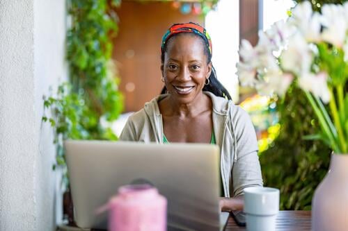 Smiling woman using laptop while sitting on the balcony people joy black natural attractive black woman happiness happy real people mature adult daily life