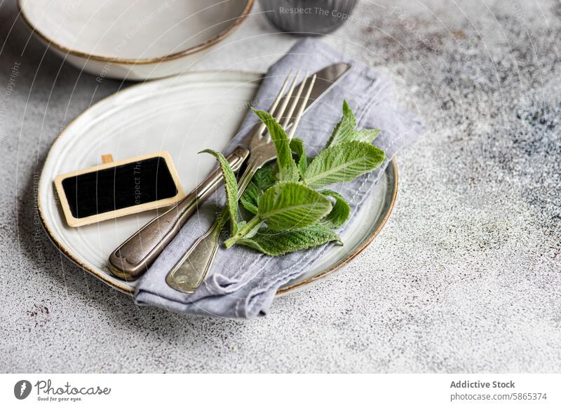 Elegant summer table setting with a fresh mint theme white ceramic plate leaves vintage silverware chalkboard gray linen napkin textured surface elegance dining