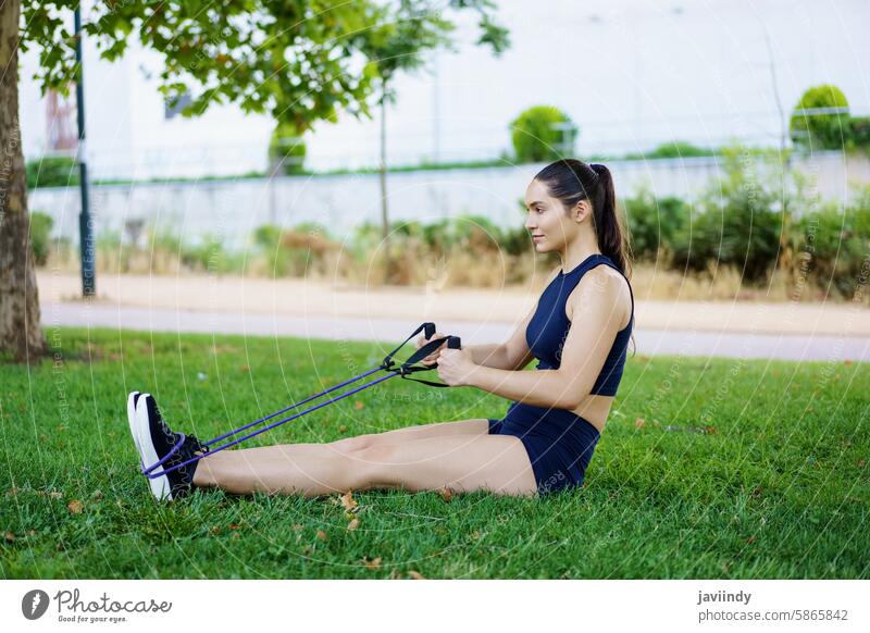 A young woman works out in the park with resistance bands, displaying her determination and commitment to fitness active activewear aerobics athlete athletic