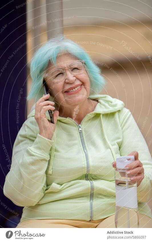 Elderly woman with teal hair talking on phone in the park elderly grandma smartphone smiling speak sitting phone call water bottle sporty attire outdoor happy