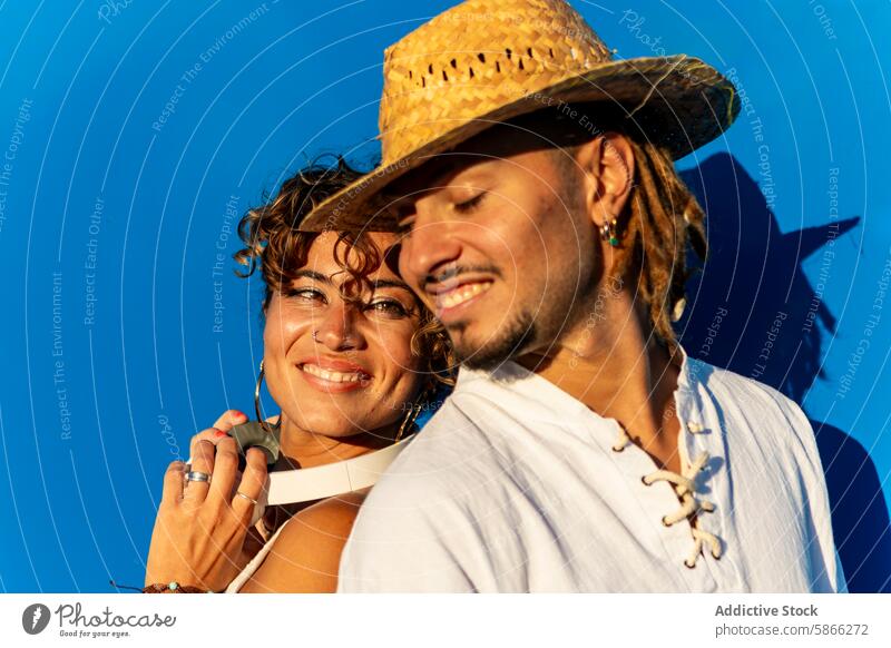 Joyful couple enjoying each other's company against blue sky smile hat caucasian woman dreadlocks accessory happiness togetherness affection outdoor vibrant