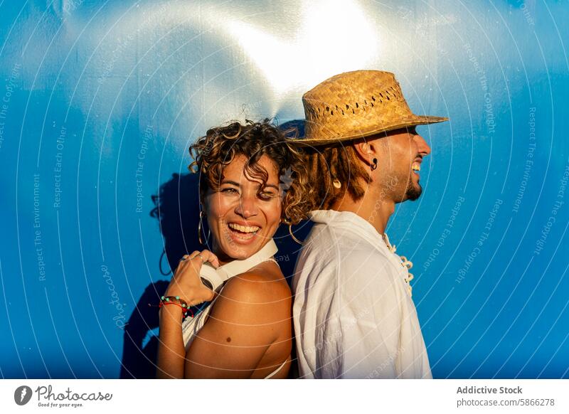 Joyous man and woman against vibrant blue backdrop blue background caucasian dreadlocks smile joy laughter gaze camera play sunlight shadow summer happy