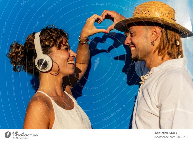 Joyful couple forming heart shape against blue wall joy blue background man woman caucasian smile dreadlocks curly hair happiness looking at each other vibrant