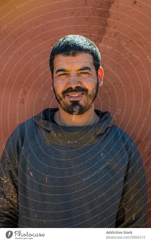 Moroccan man in a work-smeared hoodie smiling at the camera smile moroccan worker dust genuine terracotta wall sunlight warm craftsmanship labor cheerful