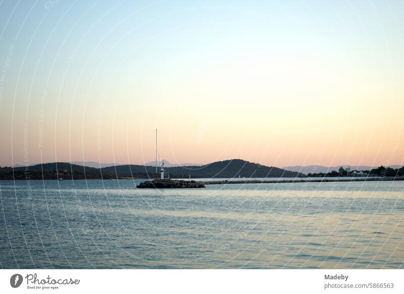 Romantic evening atmosphere at the sea with the light of the evening sun with lighthouse and pier at the harbor in the bay of Ayvalik at the Aegean Sea in the province of Balikesir in Turkey