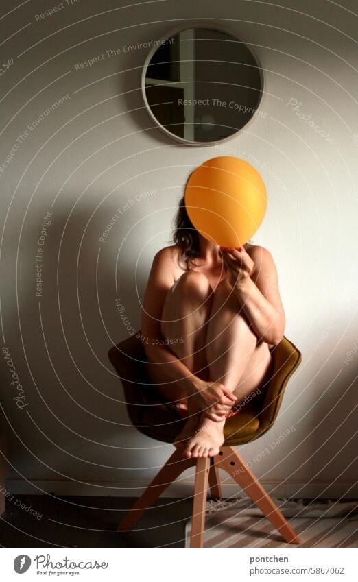 a woman without clothes sits on a chair and holds a yellow balloon in front of her face. privacy Anonymous Hide Woman hide sb./sth. secret Safety Chair Balloon