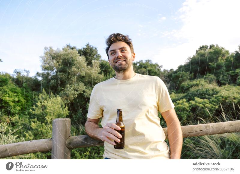 Man enjoying beer outdoors in nature man fence smiling young male adult beverage alcohol casual shirt summer day happy leisure lifestyle relaxing enjoyment