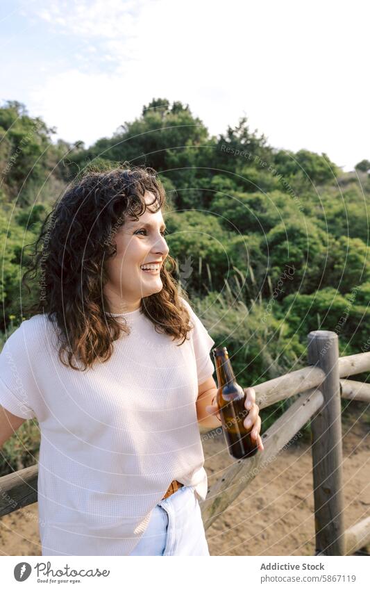 Woman enjoying a beer in nature, smiling happily woman smile happy beverage alcohol outdoor friend meeting relax leisure environment lush green bottle hold