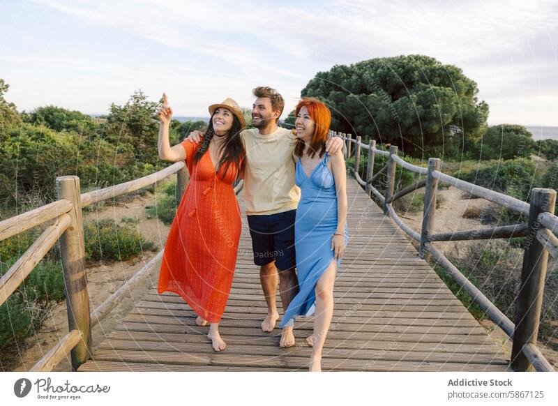 Three friends enjoy a scenic walk on a wooden pathway nature boardwalk woman chat outdoor leisure visible casual clothing summer dress sunset joyful happy