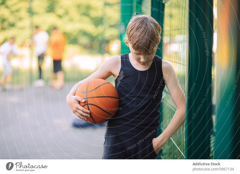 Young teenager holding a basketball outdoors athletic sport boy court play fence green game leisure young youth summer standing casual focus soft background