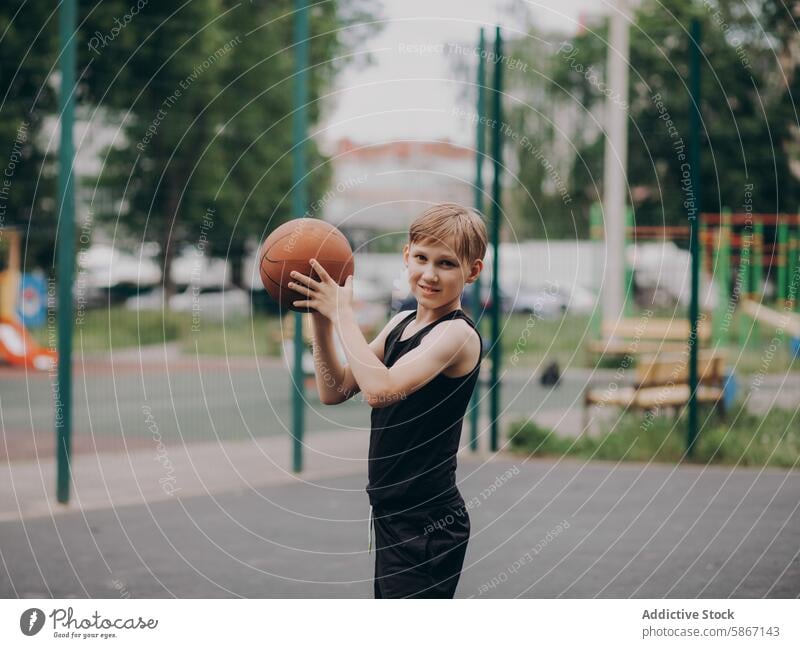 Young teenager smiling while playing basketball outdoors court sport urban park playground healthy activity fitness game sportswear leisure recreation fun