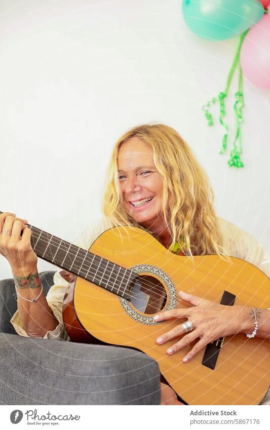 Joyful mature woman playing guitar at a festive occasion music joy party balloons celebration happiness cheerful acoustic instrument elderly blonde expression