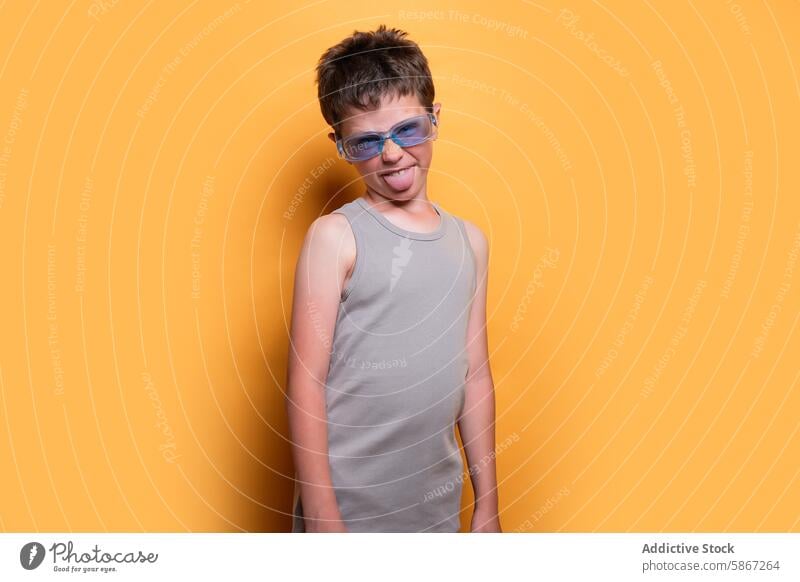 Young boy enjoying summer vibes in a studio setting child playful fun young pose orange background glasses tongue out expression sunny joyful cheerful