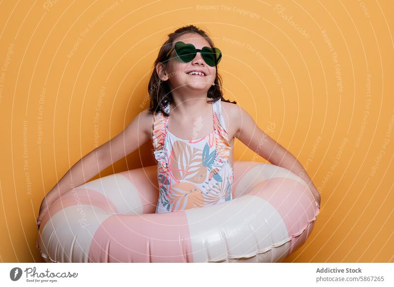 Girl with summer swimwear and sunglasses in studio girl inflatable ring orange backdrop smiling young child floral heart-shaped happy cheerful seasonal