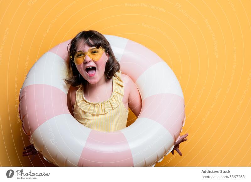 Joyful child with swim ring in a summer themed studio joyful girl sunglasses swimsuit yellow background photo shoot cheerful vibrant young fun happiness