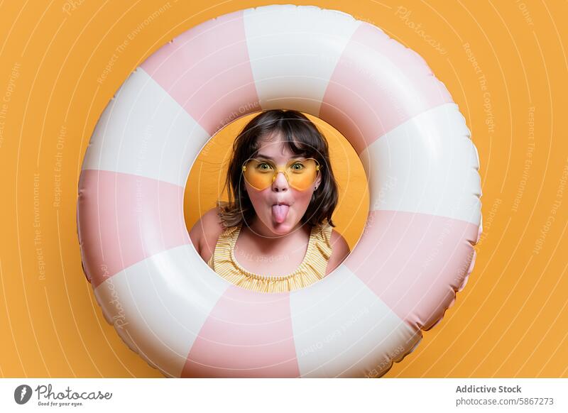 Young girl with swim ring and sunglasses on summer backdrop child playful tongue out orange background fun bright seasonal cheer vacation young portrait studio