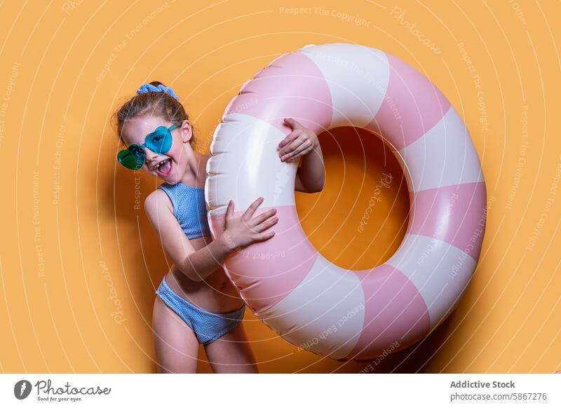 Girl with pink float in summer-themed studio shoot girl swim ring sunglasses swimsuit yellow background joy fun vibrant cheerful playful child indoor swimwear