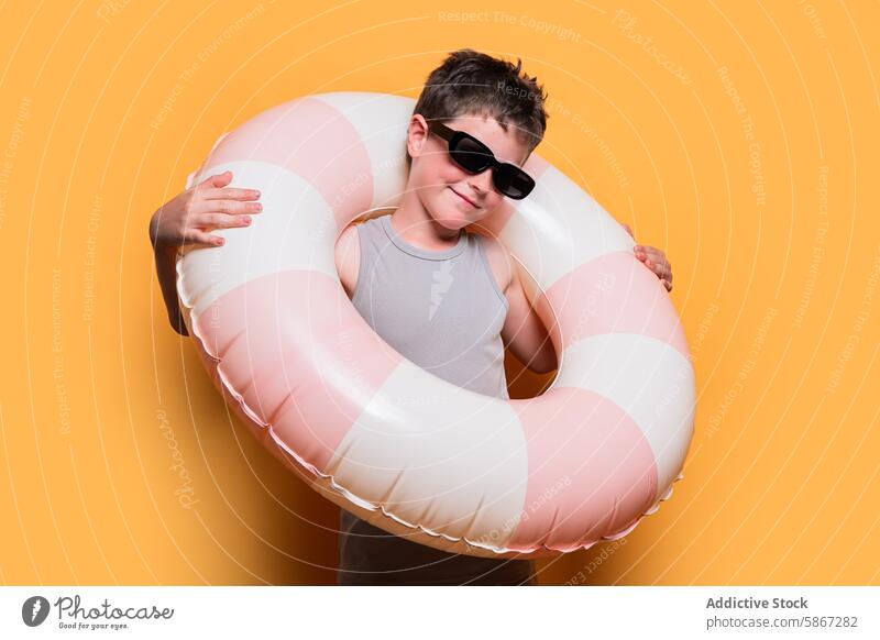 Boy with inflatable swim ring on orange background boy summer smile sunglasses studio tank top striped accessory portrait fun happy joy playful childhood