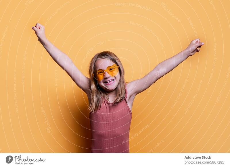 Young girl celebrating summer fun in studio child theme cheerful celebration orange sunglasses pink top bright yellow background smile joy happiness enthusiasm