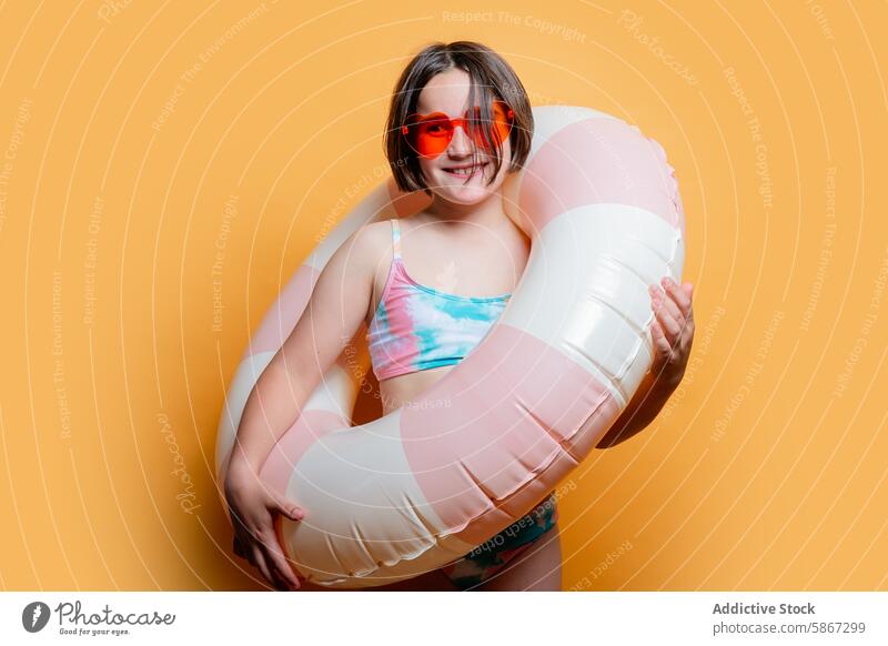 Young girl with swim ring in a summer-themed studio shoot orange background inflatable swimsuit sunglasses playful cheerful child youth kid photography model