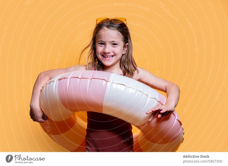 Young girl with inflatable ring in summer studio shoot yellow background playful cheerful smile sunglasses child pose radiant carefree vibe young fashion