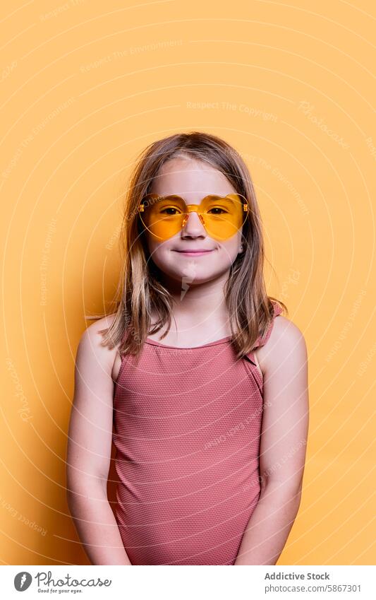 Young girl in sunglasses on a vibrant yellow background summer cheerful playful portrait studio child fashion casual color warm joyful season sunny light bright