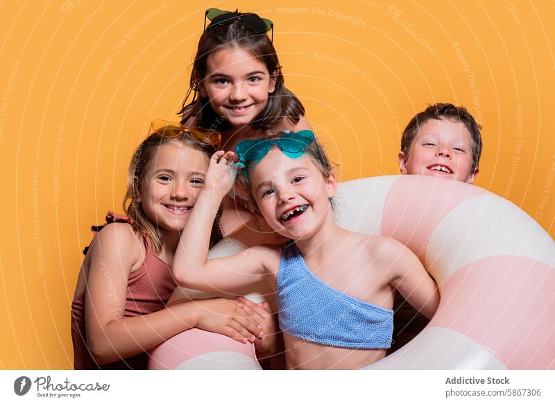 Happy children with summer props in a studio setting inflatable ring joyful pose background yellow cheerful girl boy swimwear sunglasses smile friendship group