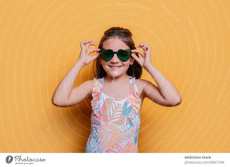 Young girl in swimsuit and sunglasses in studio child summer theme cheerful pose yellow background vibrant tropical print fashion style colorful brightness