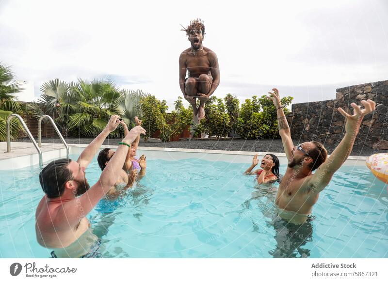 Friends cheering as man jumps into swimming pool summer friends cheerful jumping water outdoor fun laugh poolside excitement women diverse multiethnic group sun