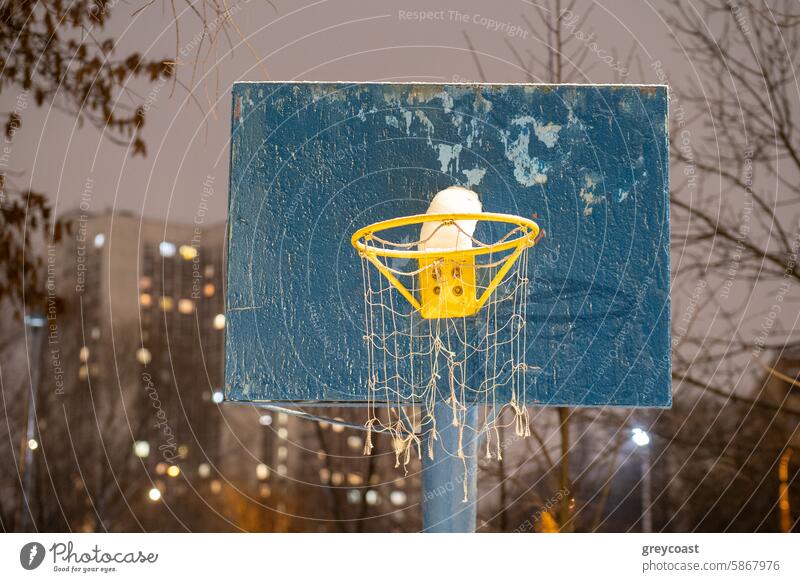 Basketball hoop with snow at night basketball urban background winter cold covered city sport net game season frost park blue backboard yellow rim nighttime