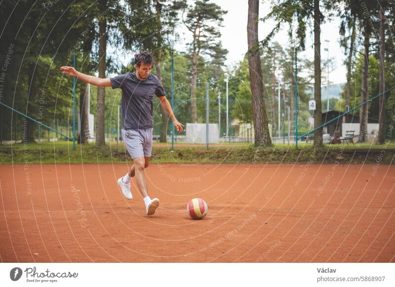 Soccer player in 20s plays with a balloon on a clay court. Amateur sport. Individual football training. Soccer. Kicking, striking, passing and dribbling soccer