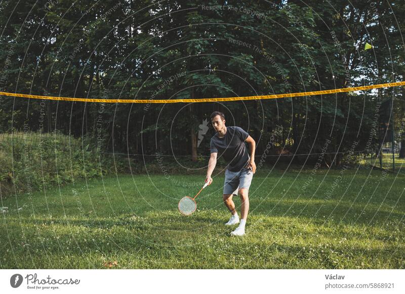 Black-haired badminton player practices his strokes on the grass court. Individual technique training. Amateur concept of the sport. The joy of the game athlete