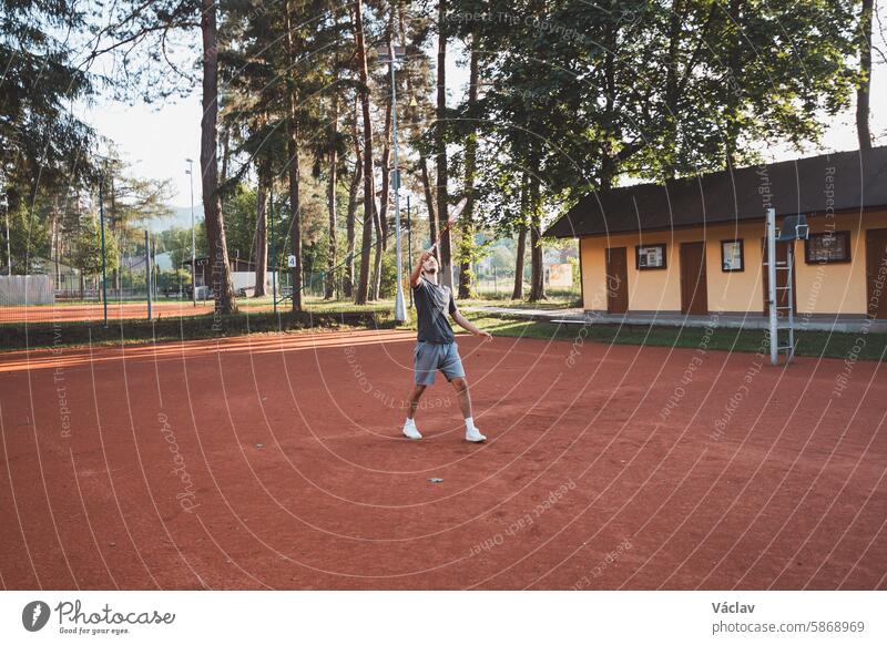 Black-haired athlete with a smile on his face plays badminton on a clay court. Enthusiasm for amateur sport. Learning new movement skills racquet caucasian