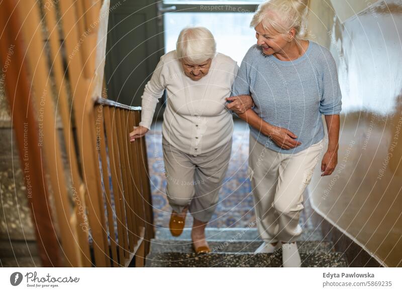 Caregiver helping an elderly woman up the stairs smiling happy enjoying positive contented people senior mature female home house old aging domestic life