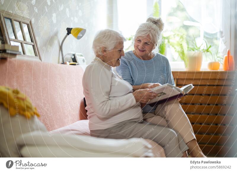 Senior woman and her adult daughter looking at photo album together smiling happy enjoying positive contented people senior mature female elderly home house old