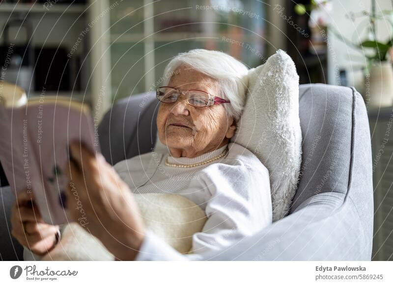 Elderly woman reading a book in a comfortable armchair at home smiling happy enjoying positive contented people senior mature female elderly house old aging