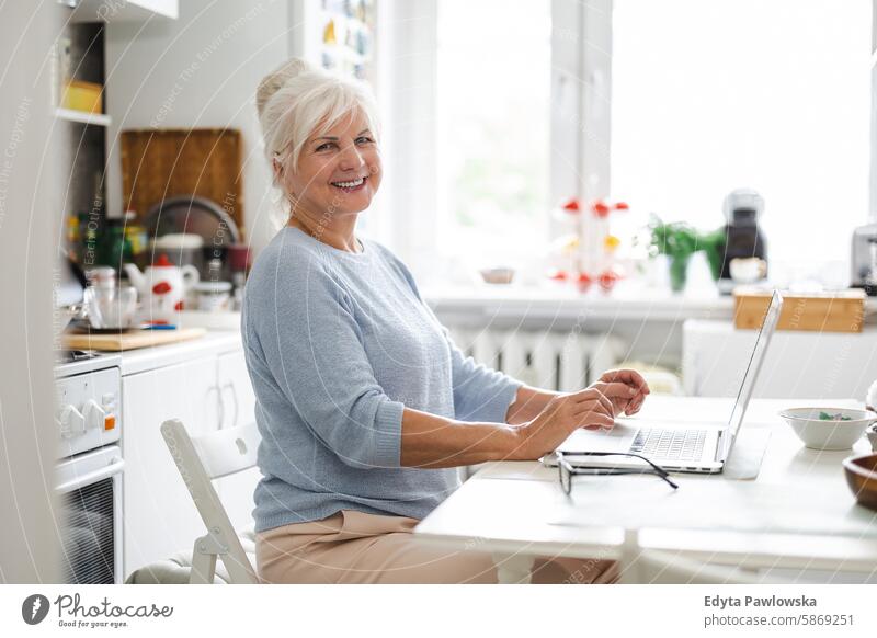 Senior woman with laptop sitting at the table in the kitchen people senior mature female elderly home house old aging domestic life grandmother pensioner