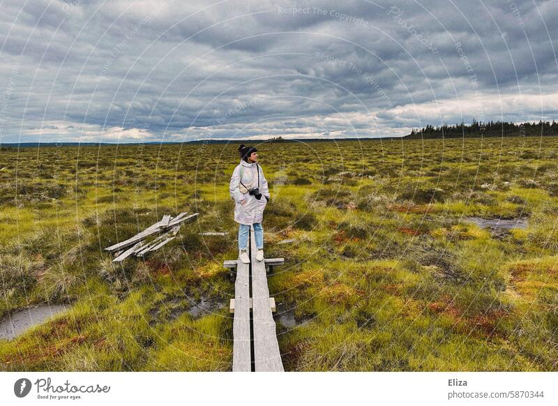 Woman with camera standing on a wooden footbridge in a moorland area Footbridge cloudy sky hike Landscape Nature Bog Lanes & trails Trip Nature reserve Marsh
