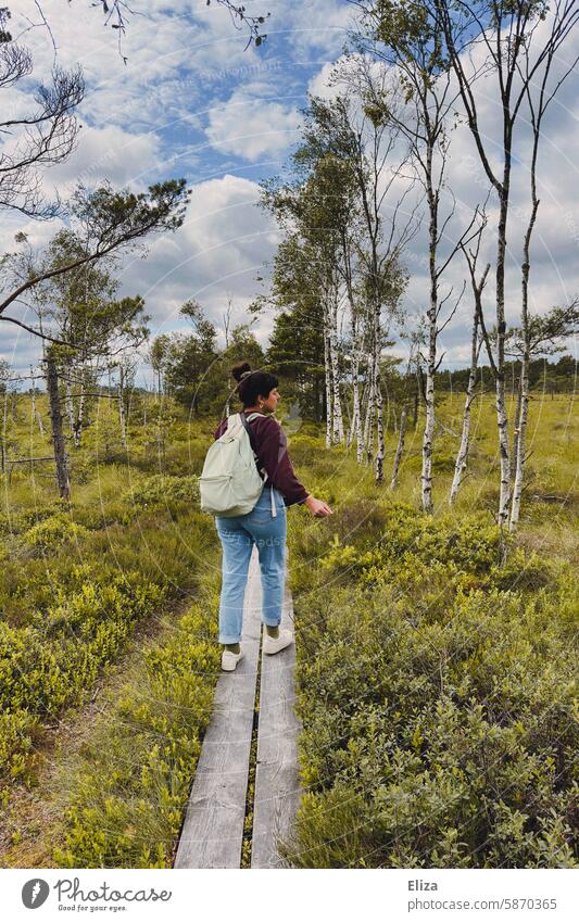 A woman with a rucksack walks along a footbridge through nature Nature Woman To go for a walk Footbridge birches Forest trees hike Bog Landscape Nature reserve