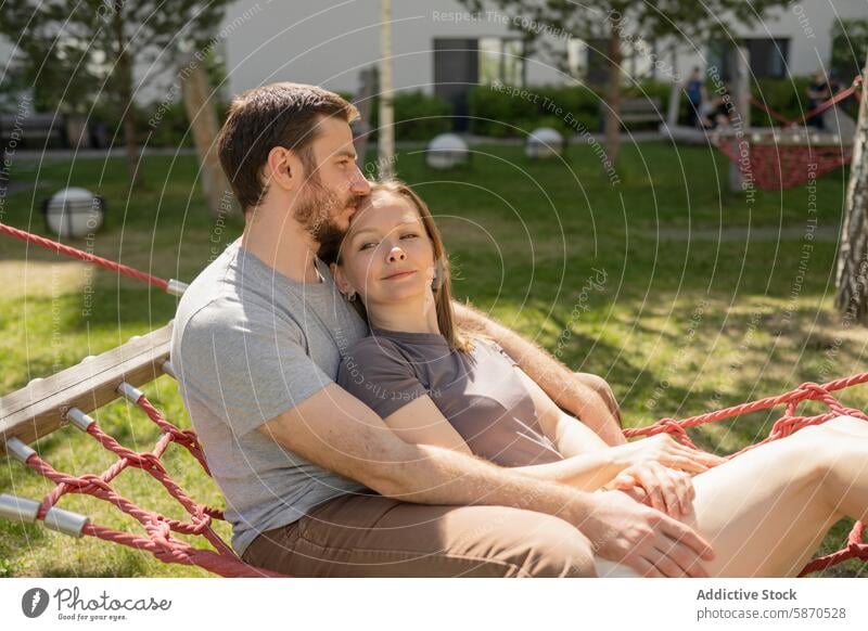 Couple relaxing together on a park hammock couple man woman summer comfort affection gaze trees outdoors leisure happiness love bonding serene sunny grass