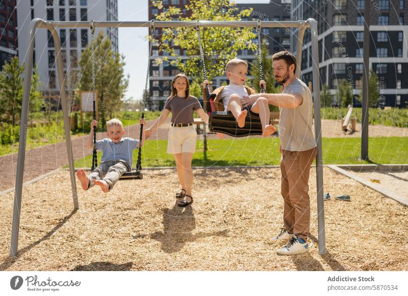 Family enjoying time together at the park family summer swing child toddler father mother son smiling playing outdoor sunshine daytime leisure recreation