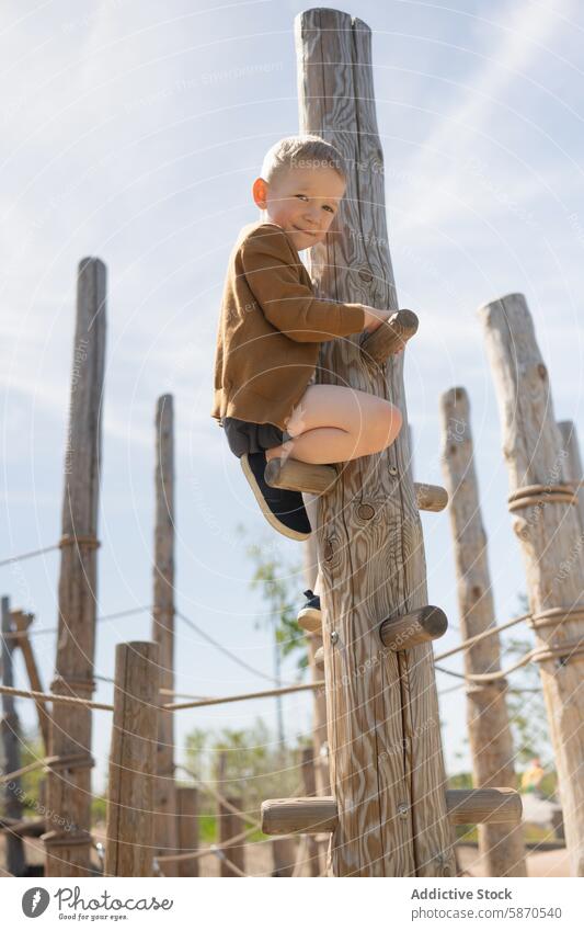 Young boy climbing at a playground during summer outdoor fun activity joyful child wooden structure park kid recreation active adventure sunny daylight youth