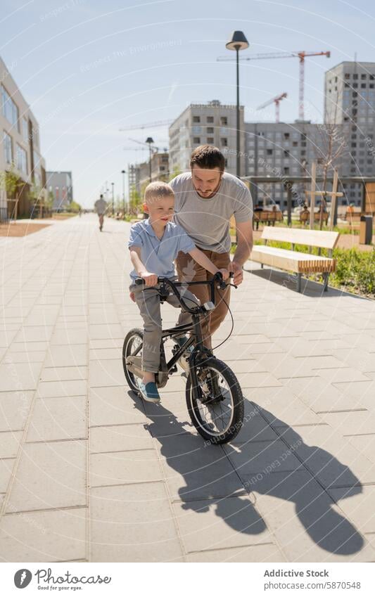 Father teaching son to ride a bike in urban park father bicycle learning male adult child summer outdoors city activity family bonding street sidewalk guidance