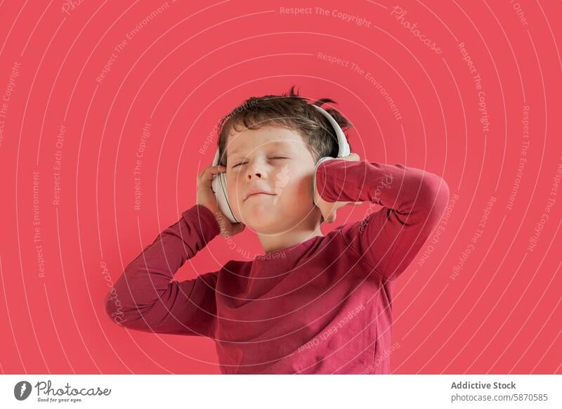 Young boy enjoying music with headphones on red background kid child male studio listening smile happy leisure entertainment eyes closed technology gadget