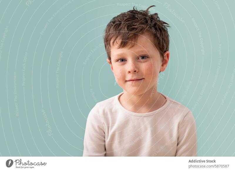 Young boy looking at camera in studio setting kid child young male close-up headshot portrait eye contact caucasian smile soft gentle light shirt beige