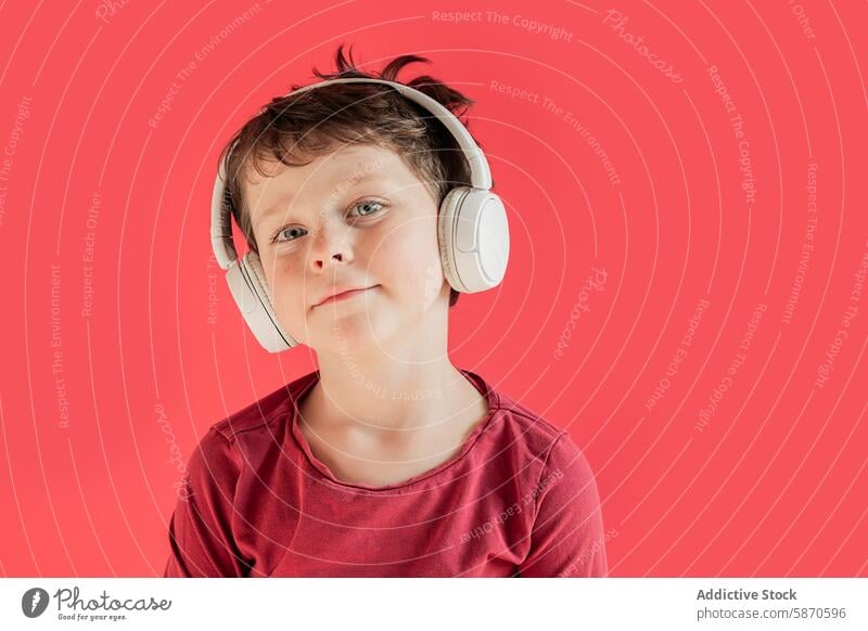 Young boy wearing headphones in a studio setting kid music technology gadget device listening red background portrait youth child male casual leisure audio