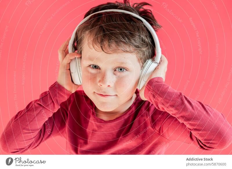 Boy wearing headphones in a bright studio setting boy looking at camera child technology device gadget red background maroon shirt subtle smile portrait music