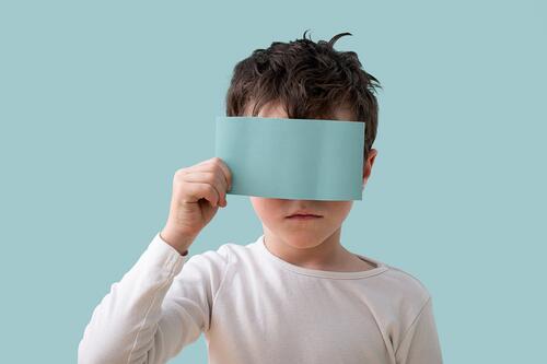 Young boy holding a blue card over his face in studio face covered white shirt caucasian light blue background portrait simplicity expression posture child kid