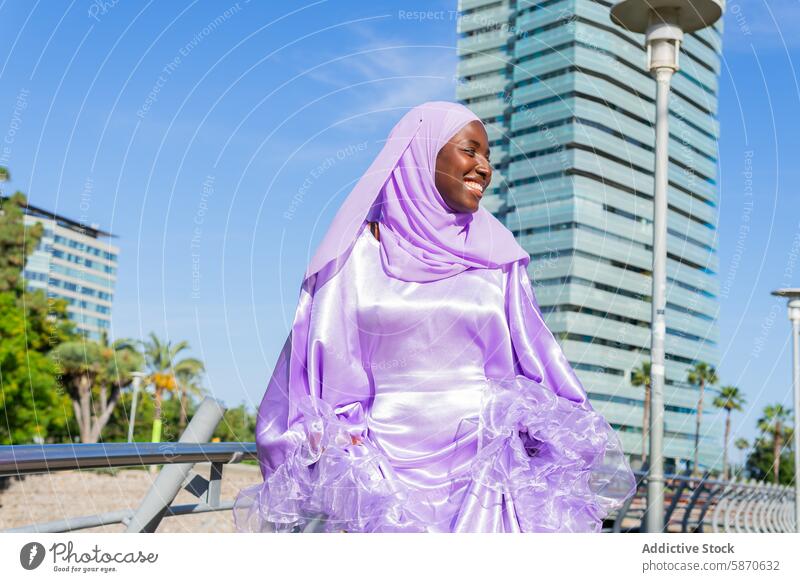 Smiling woman in purple hijab enjoying urban park skyscraper smile radiant outdoors fashion modest clothing sunny day happiness positive islam muslim summer