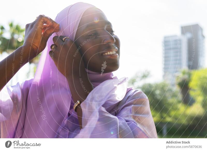 Woman in Lavender Hijab Adjusting Headscarf Outdoors park headscarf sunny cheerful warmth moment sunlight love affection outdoor woman caring bonding